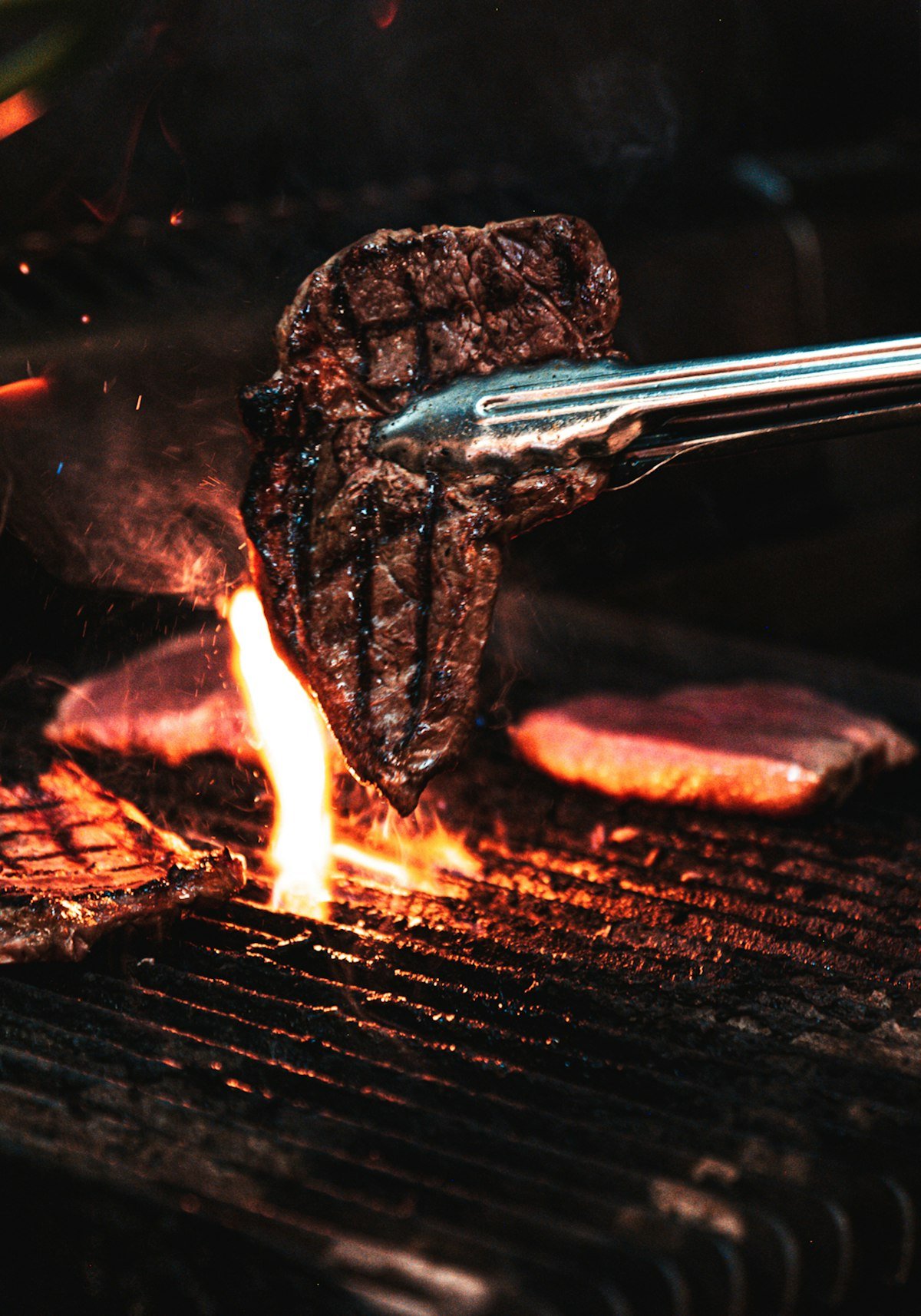 Meat searing over an open charcoal fire at night