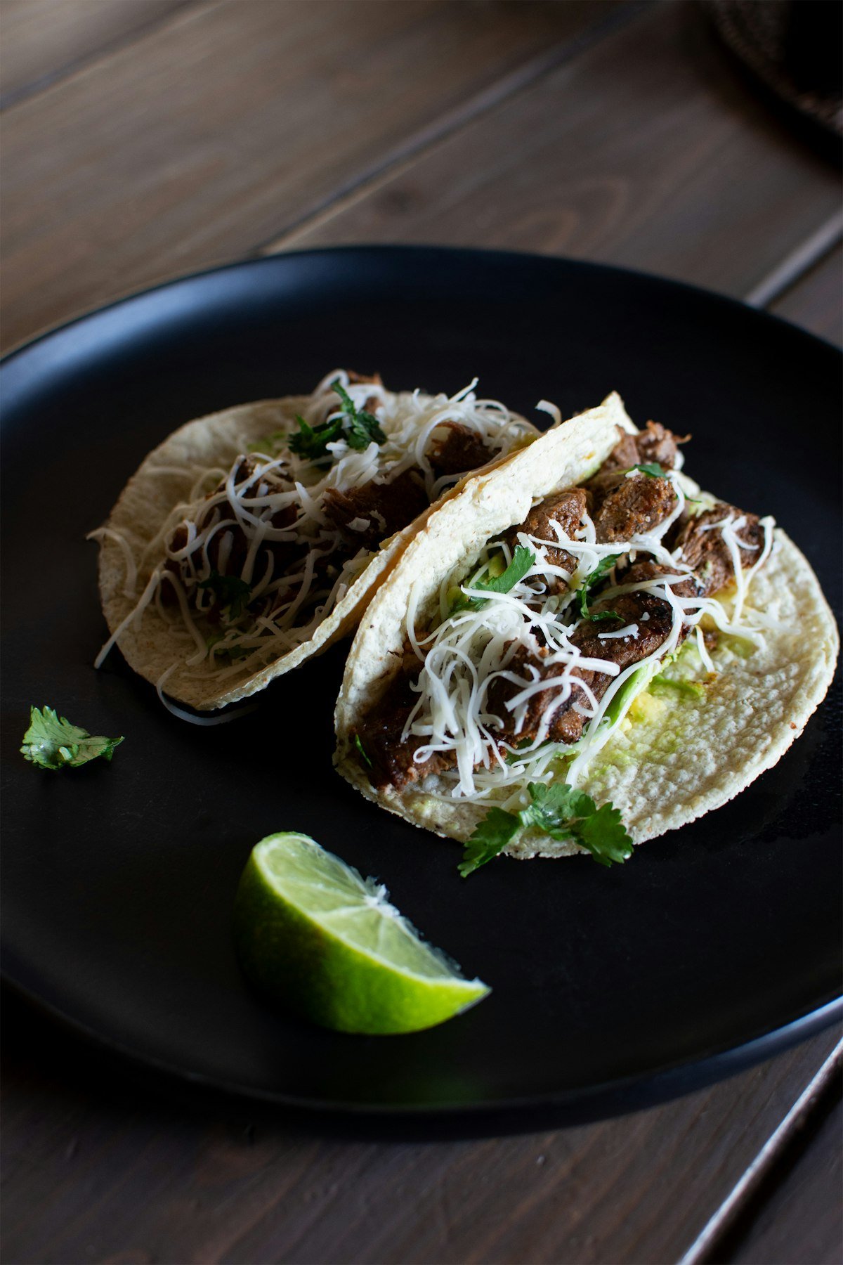 Two tacos on a dark plate with lime