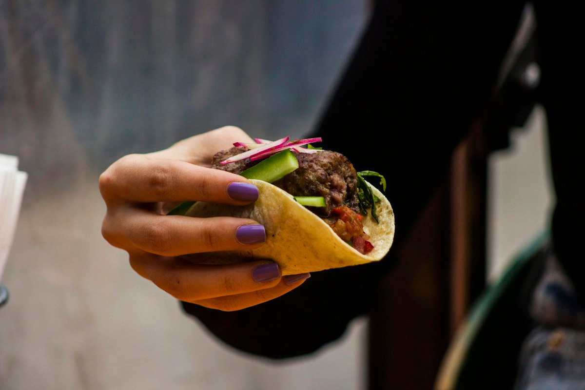 A hand holding a taco filled with meat and greens